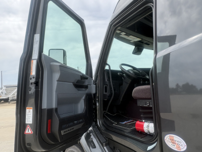 Truck cab interior view with open driver door showing dashboard and steering wheel, Mack branding on door panel.