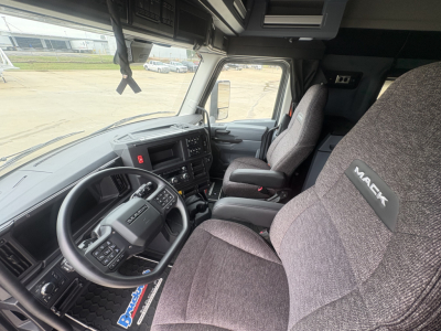 Truck cab interior showing steering wheel, dashboard, and two gray fabric seats with Mack branding on headrest in a new Mack AN64T64 conventional daycab.