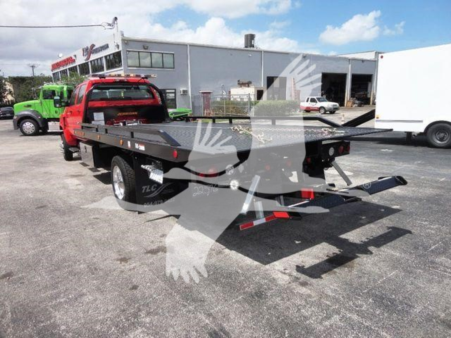 Flatbed rollback tow truck with a metal platform and ramp, red cab, in-service. visible text includes J26674 stock number and dealership background signage faintly readable.