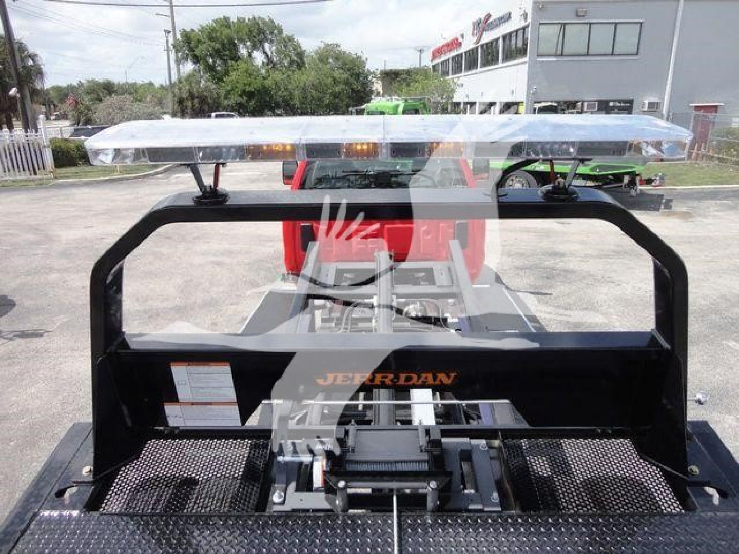 Truck bed with overhead light bar and Jerr-Dan rollback carrier showing control components and mounting in front of cab.