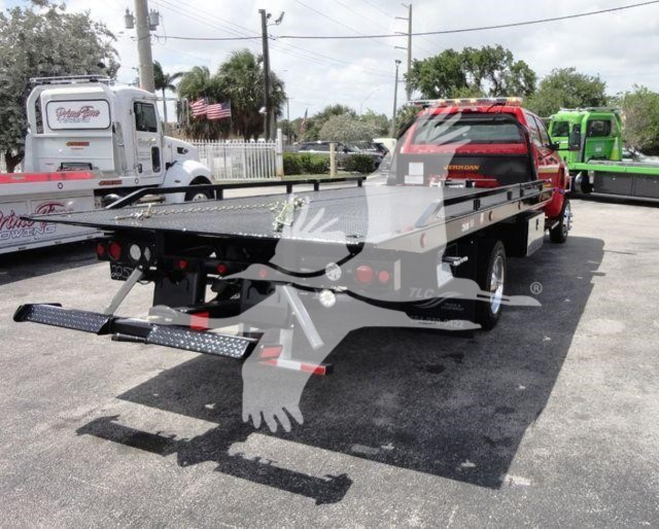 Flatbed tow truck from rear-left view showing hydraulic ramps and flatbed with chain hooks and taillights.