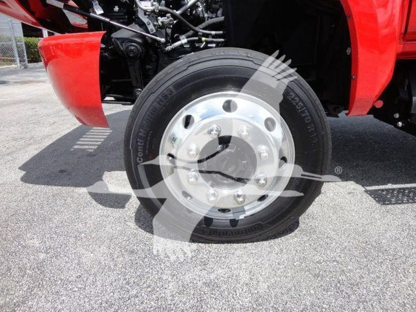 Truck front wheel showing glossy steel hubcap and tire on red International CV series, with visible suspension components.