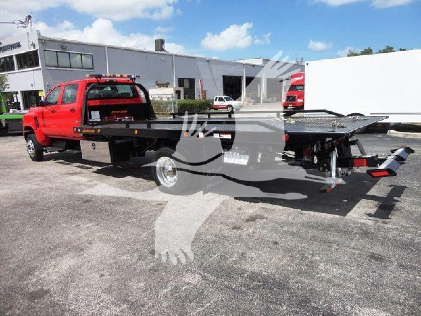 Red International CV heavy-duty rollback tow truck with a flatbed and black accents, parked outdoors near a service facility.