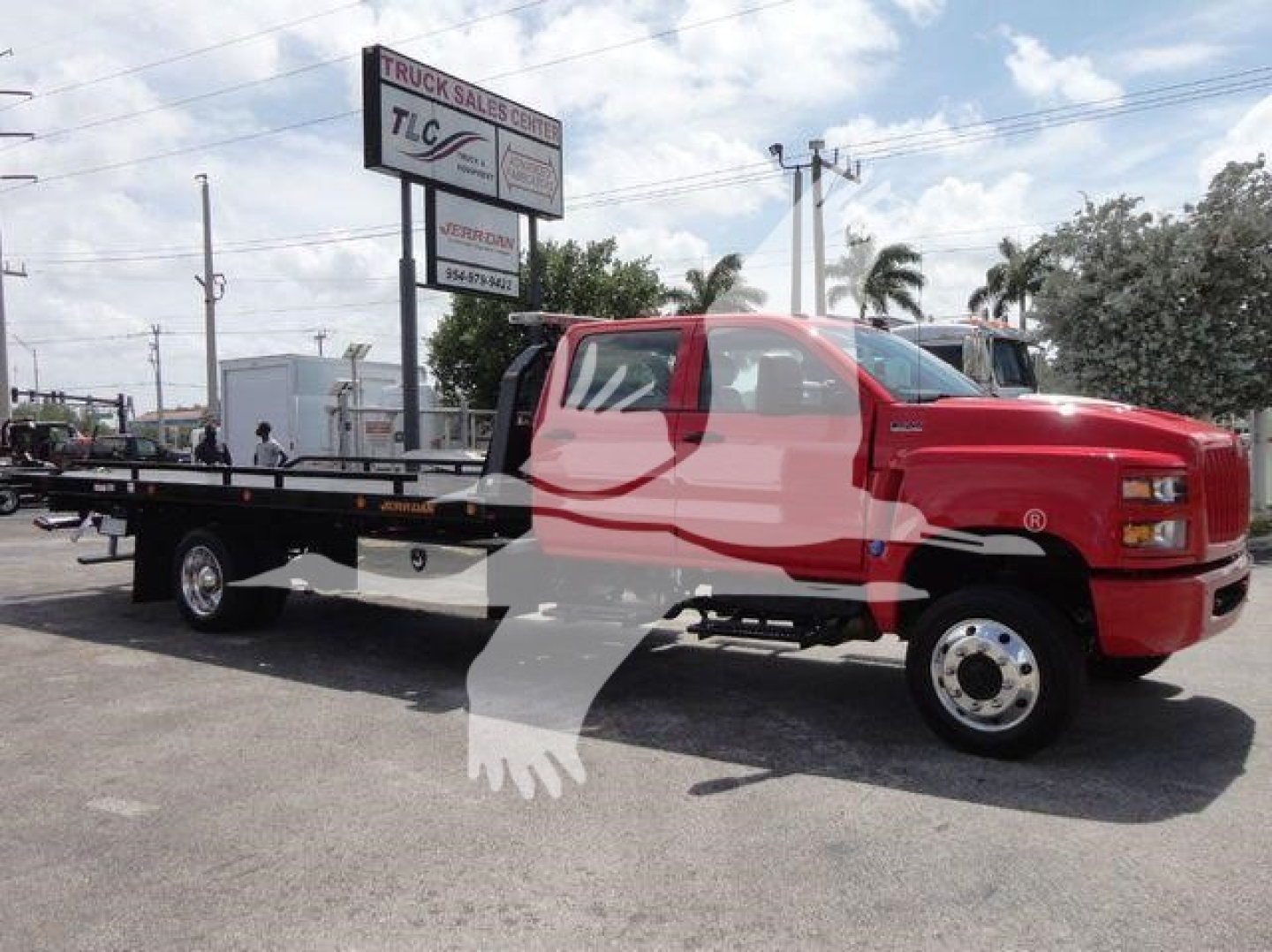 Truck: red International CV with flatbed rollback body, side view showing TLC Truck Sales Center sign in background.