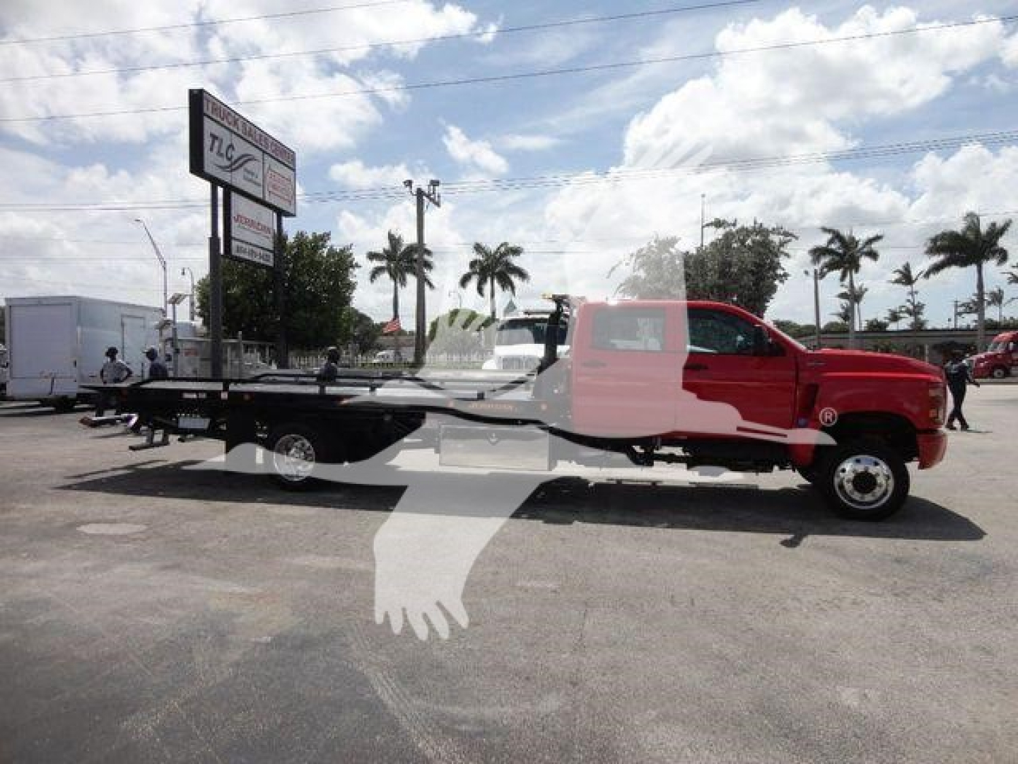 Truck in foreground with a long flatbed body and red cab under a partly cloudy sky.
