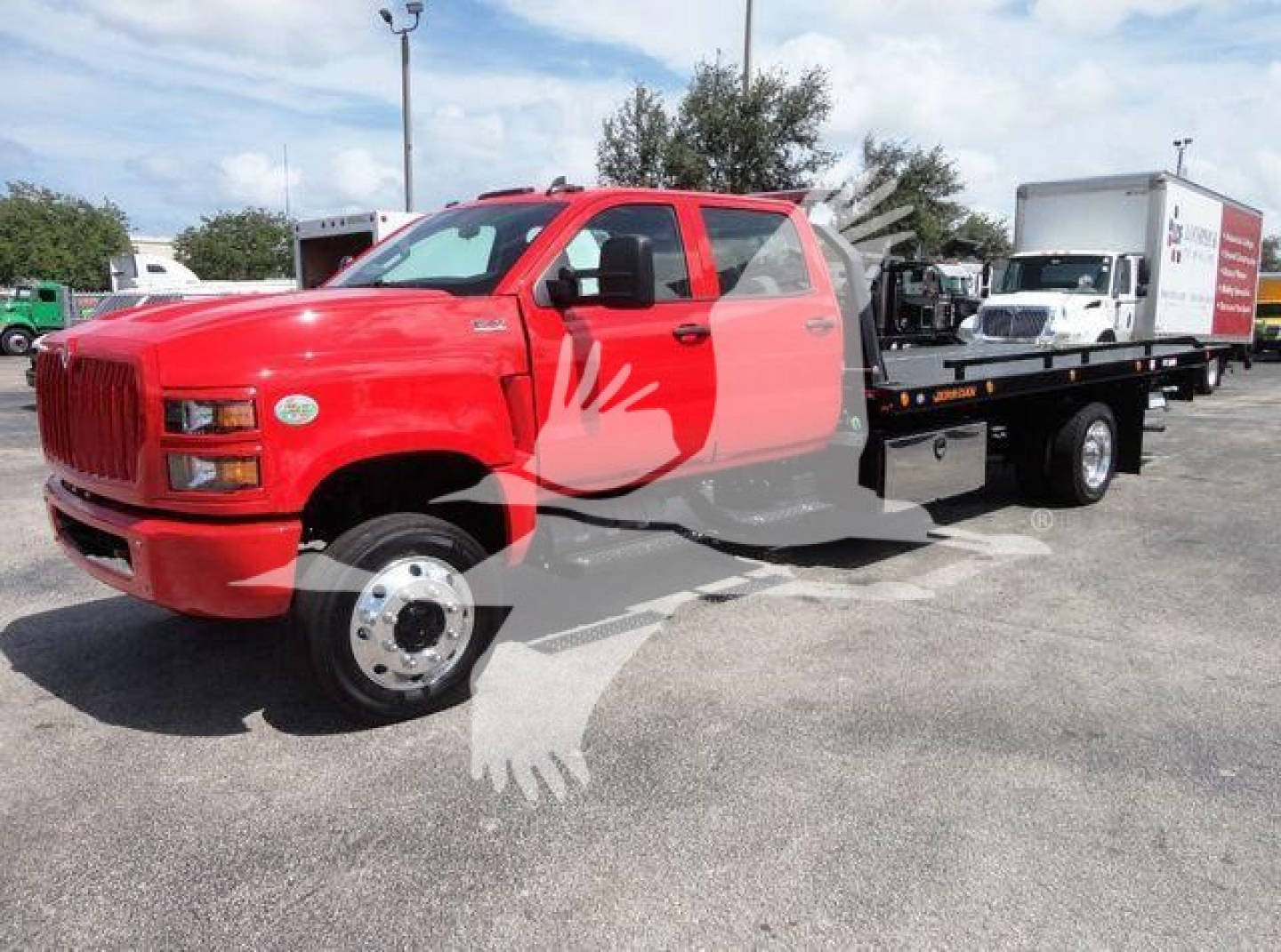 Truck with a red cab and a flatbed rollback body, International badge on grille, text on the side panels of the truck and a white trailer in the background.