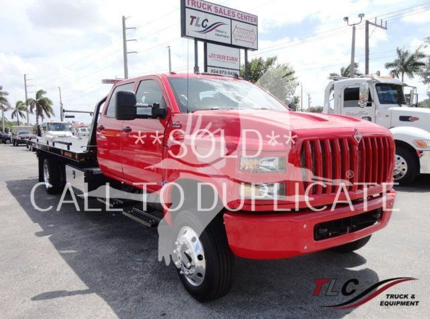 Red International tow truck with flatbed viewed from front-left, stock number J26674, TLC logo on bumper, dealership lot background.