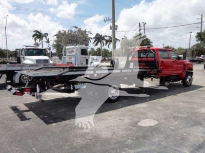 Side view of a red tow truck with a long flatbed trailer in a dealership lot.