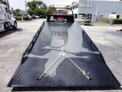 Flatbed tow truck bed with diamond plate surface and tie-down anchors; bird watermark; front cab area in background.