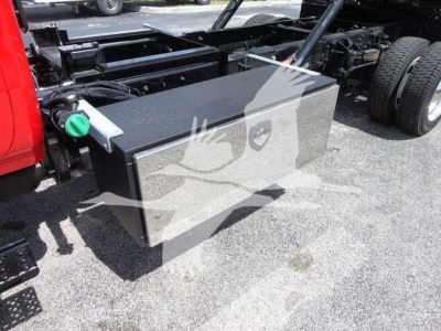 Truck chassis with large rectangular black fuel/auxiliary tank mounted under the frame on a new International CV rollback truck showing green capped fitting and surrounding hardware.