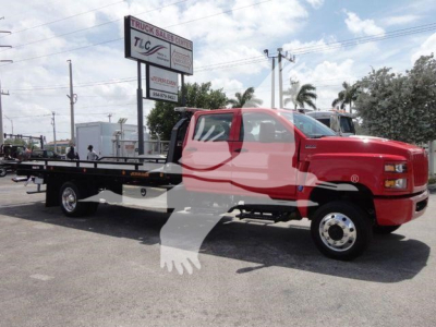 Truck: red International CV with flatbed rollback body, side view showing TLC Truck Sales Center sign in background.