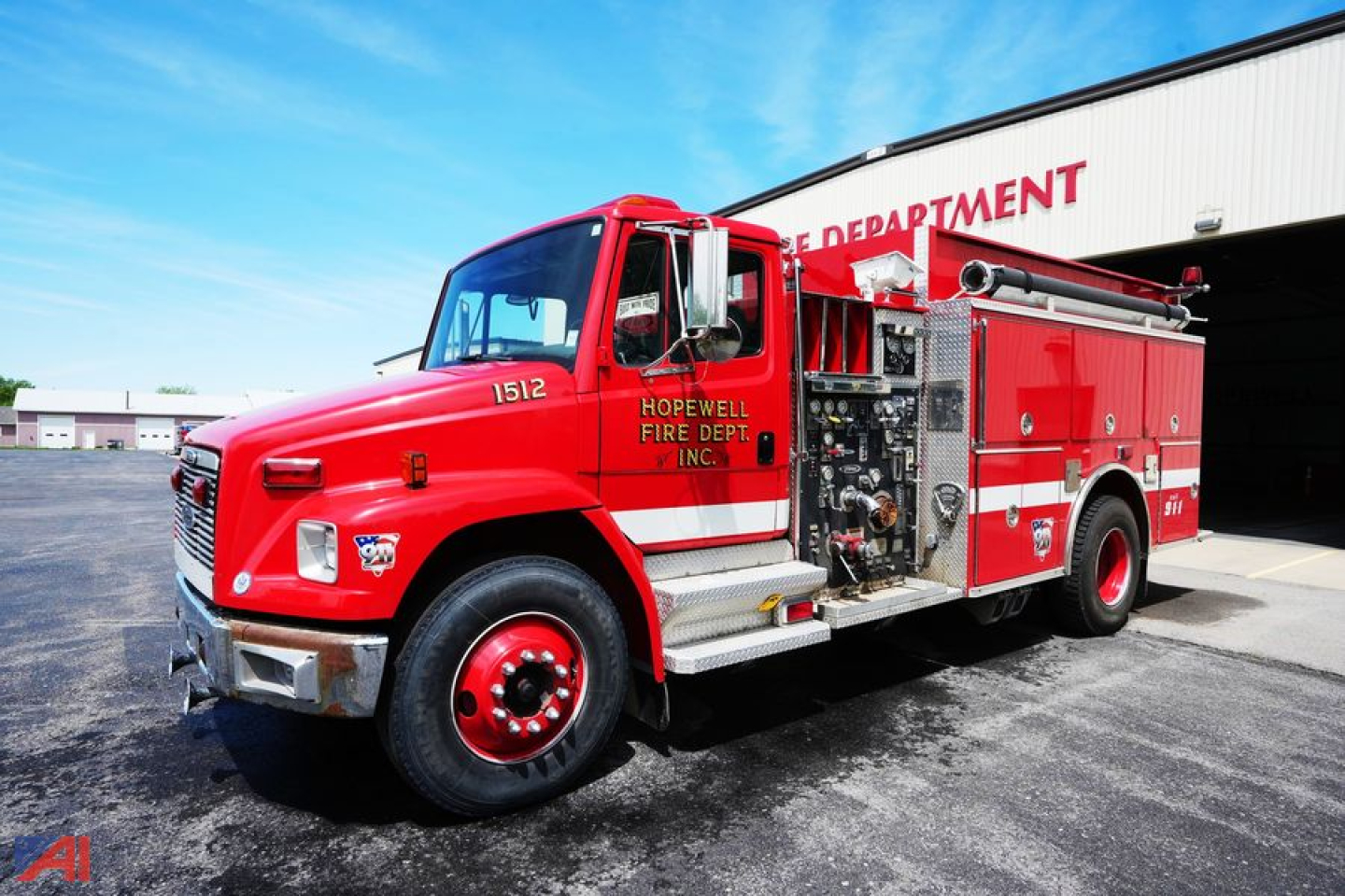 Fire engine showing a red 1998 Freightliner FL80 Pierce Saber Pumper with compartments and hoses in front of a fire department building.