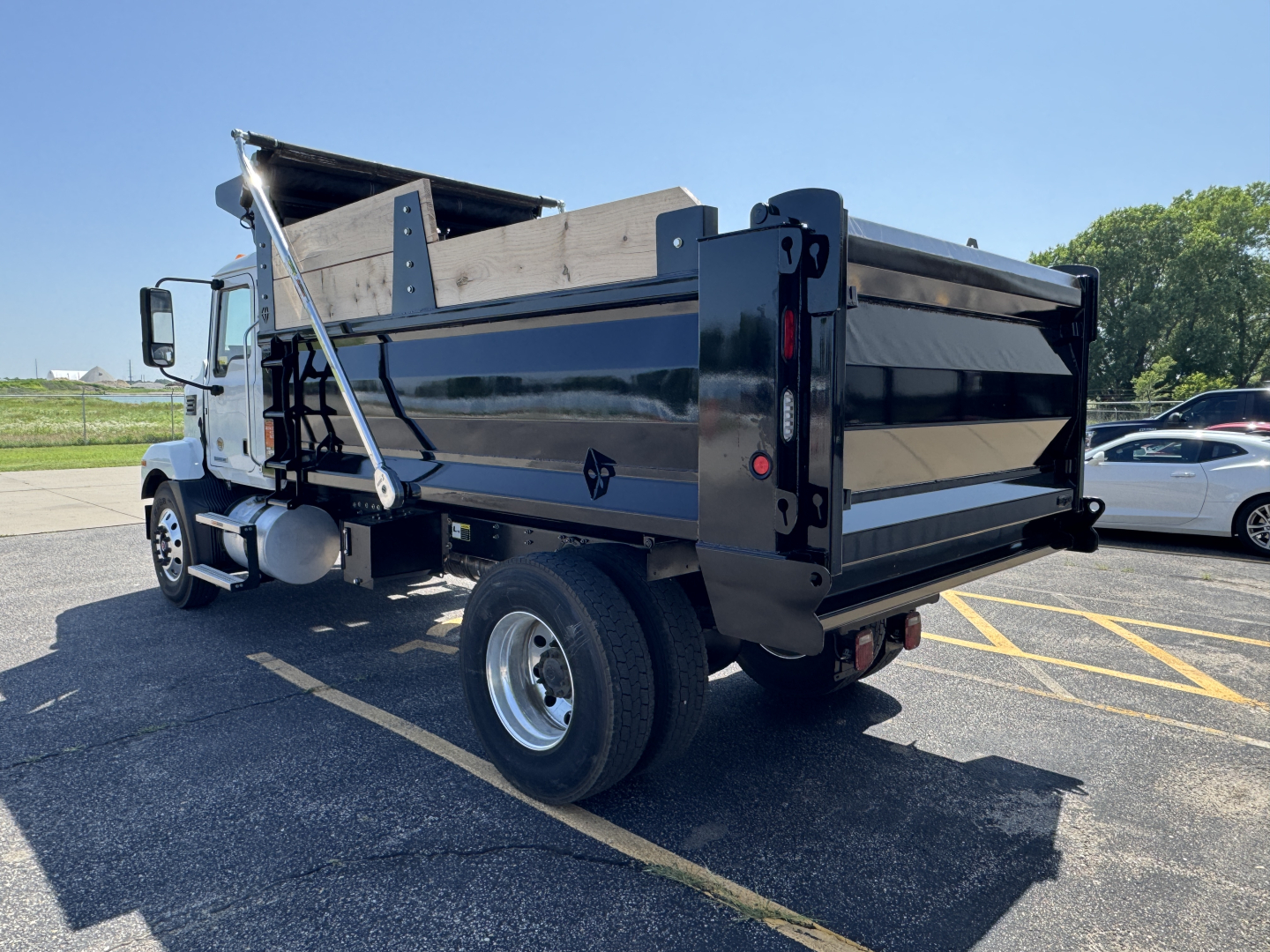 Dump truck bed of a 2025 Mack MD7 dump truck with raised hydraulic dump body and black paint, side view showing rear tailgate and wheel, VIN plate likely not visible.