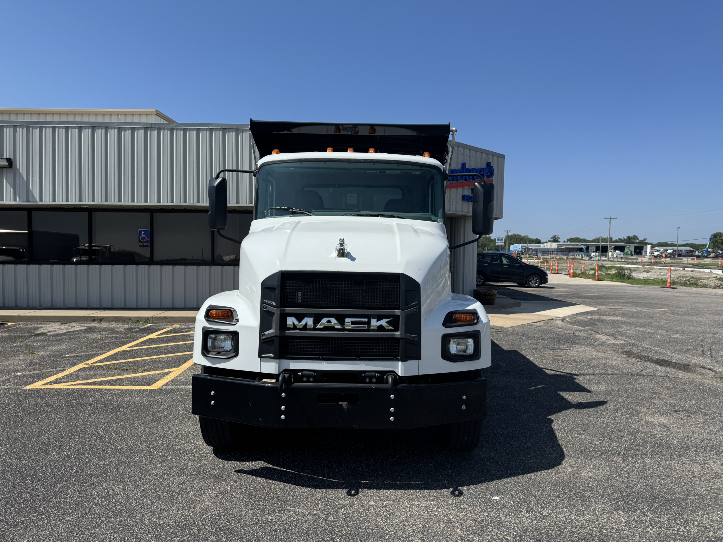 Front view of a white 2025 Mack MD7 dump truck showing grille with MACK letters, cab, headlights, and raised dump bed.