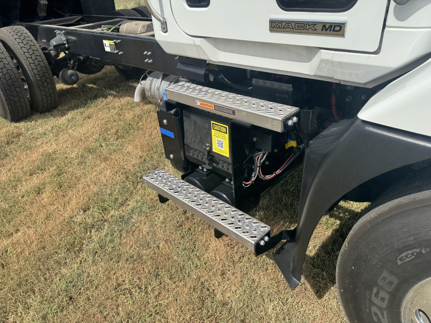 Mack MD7 truck side showing auxiliary battery/air system with diamond plate steps and wiring harness visible under cab.