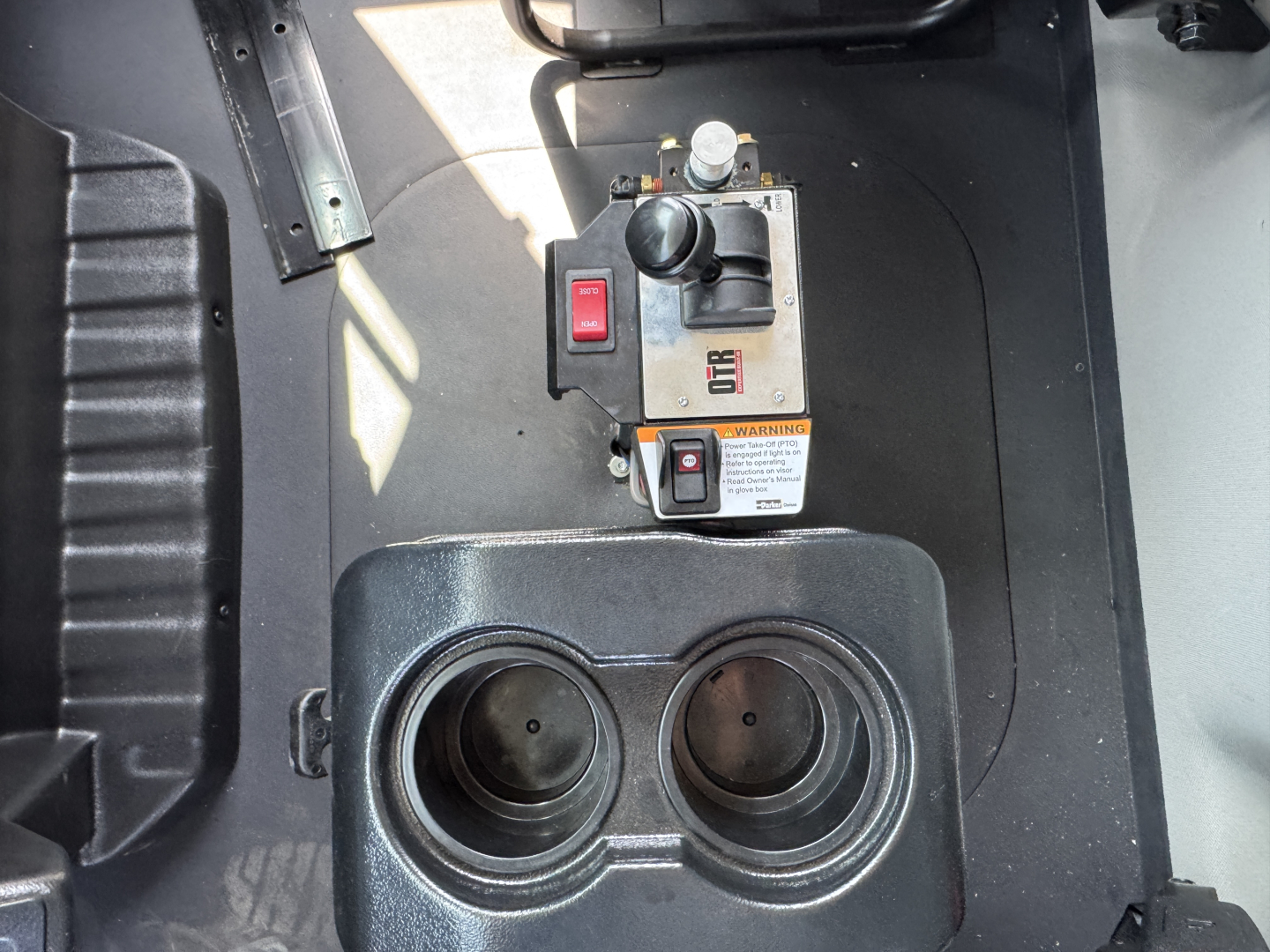 Two cup holders and a control panel in a Mack MD7 dump truck cab area with switches and warning label visible.