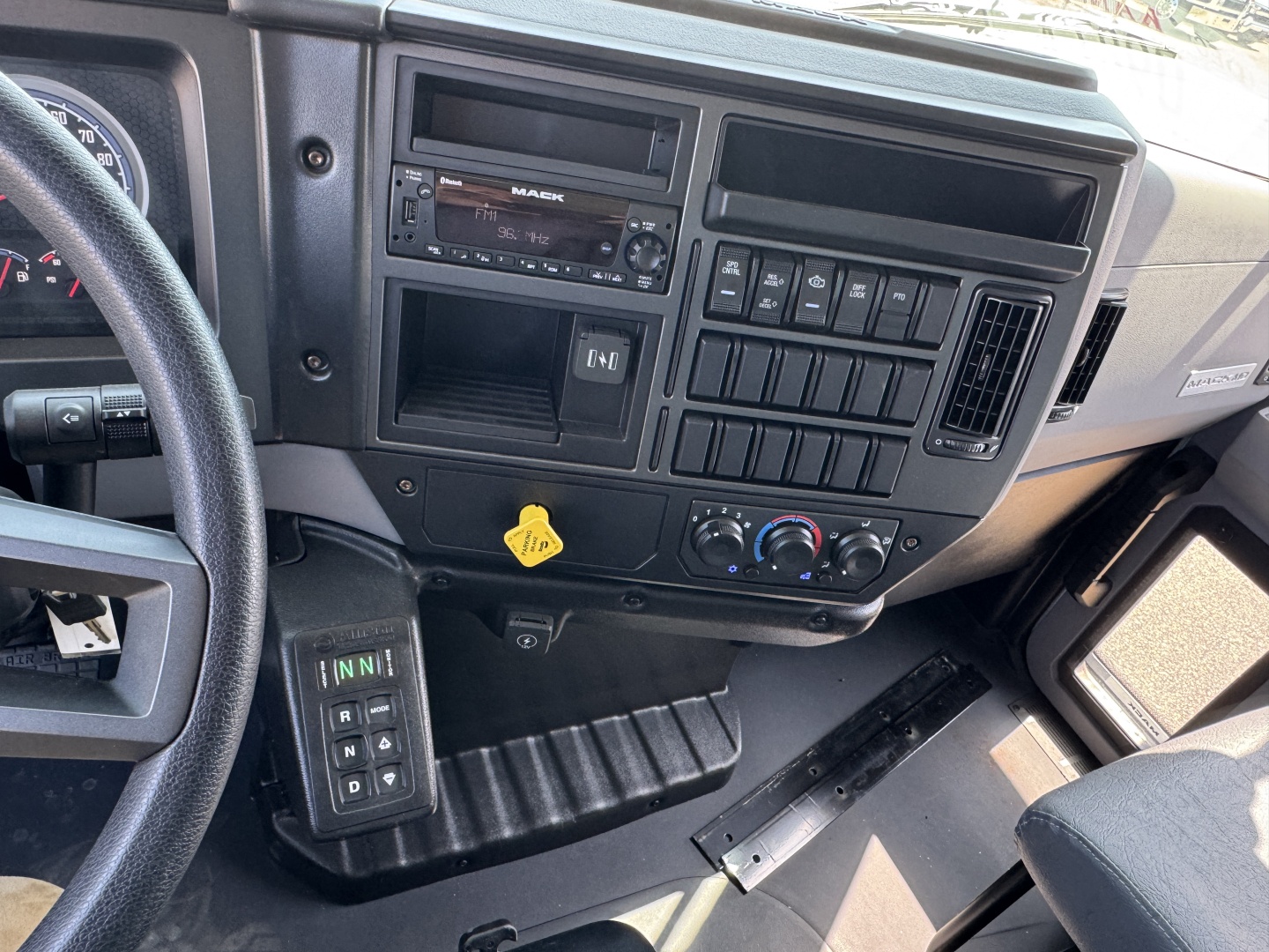 Dashboard area of a 2025 Mack MD7 truck cab showing steering wheel, radio, climate controls, and a switch panel.