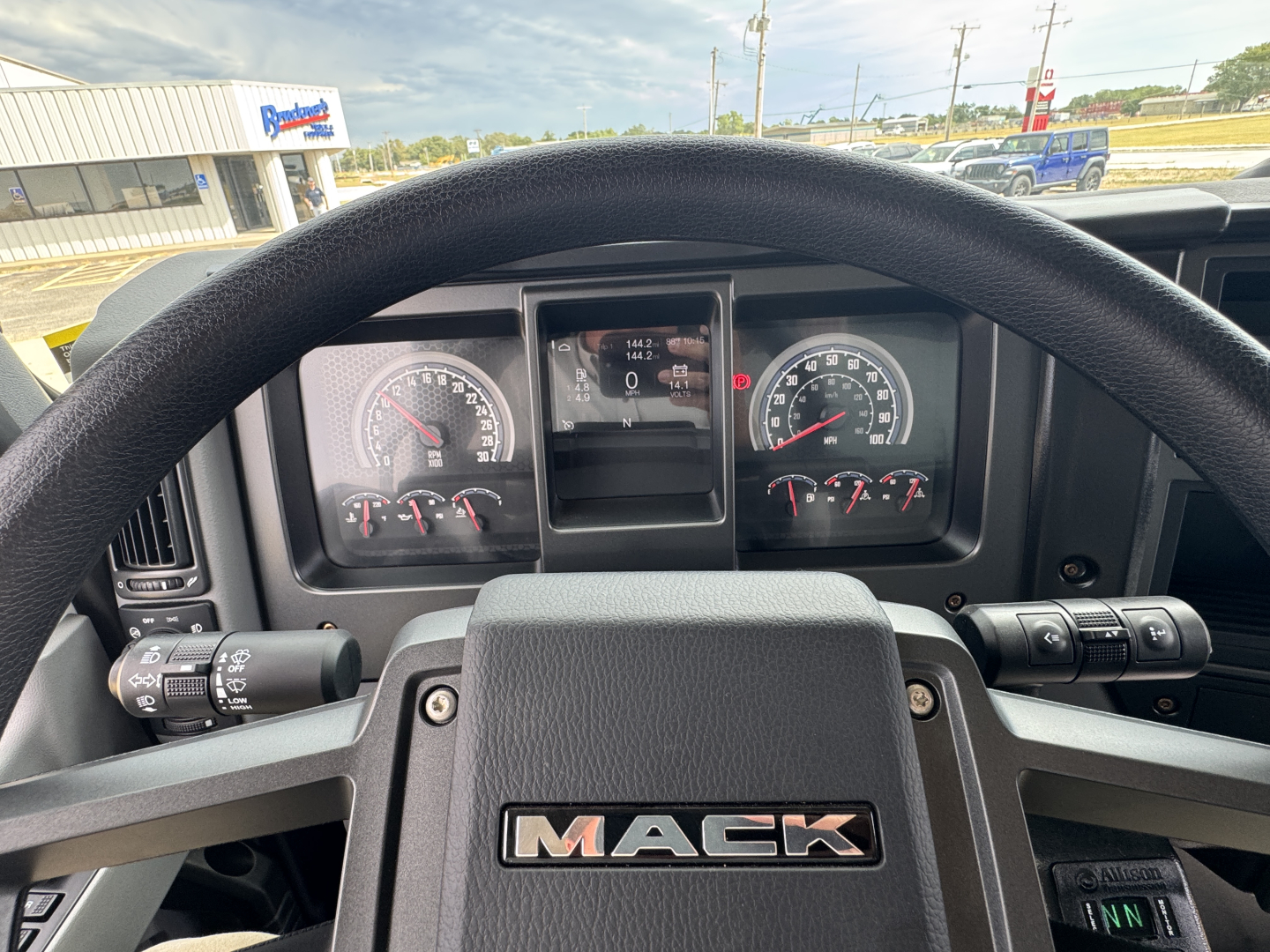 Mack MD7 truck interior dashboard view with steering wheel and instrument cluster showing gauges and a central display.