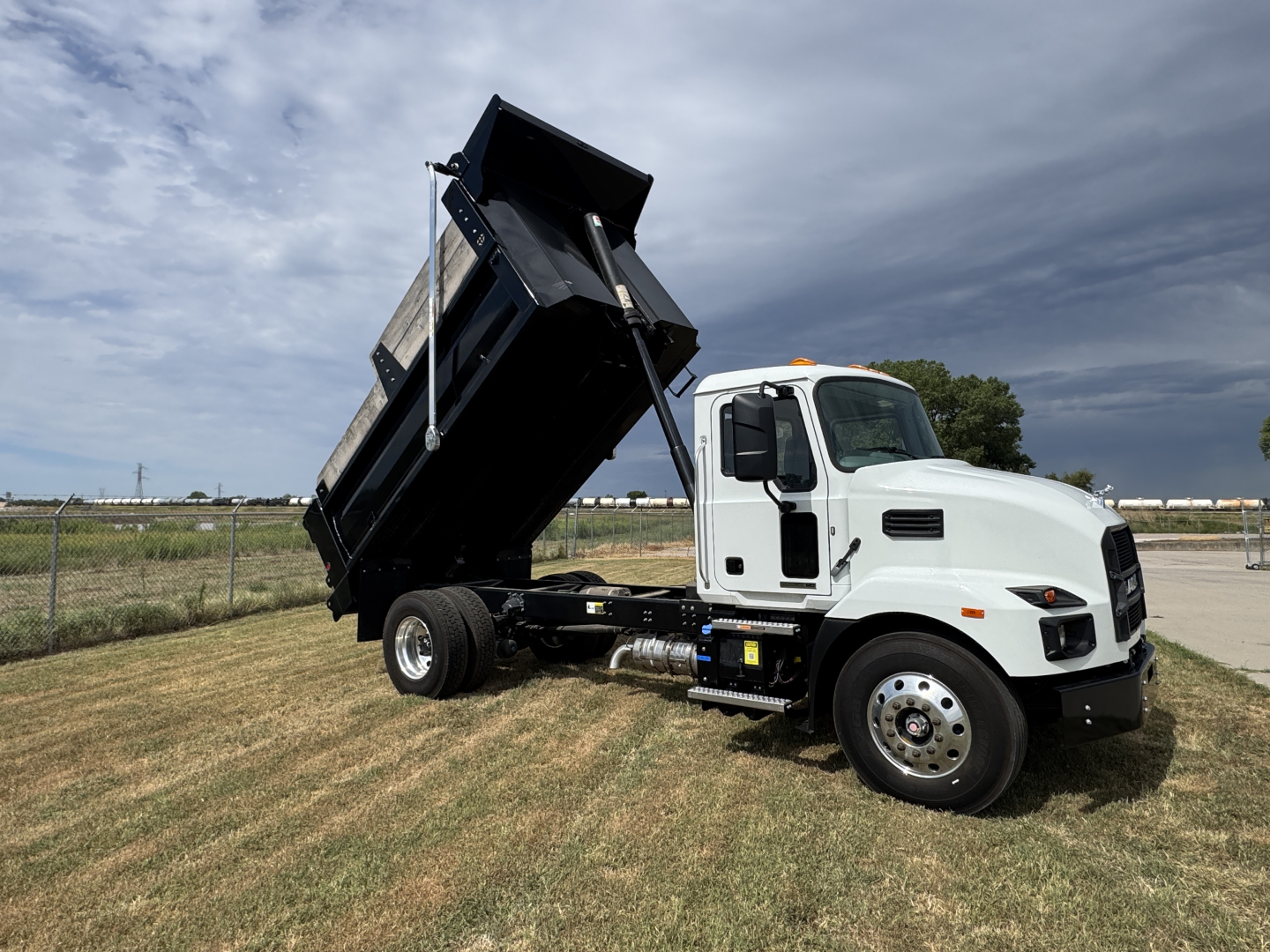 Dump truck (Mack MD7) with dumping bed raised, white cab, black dump body, side view showing hydraulic system and front wheels.