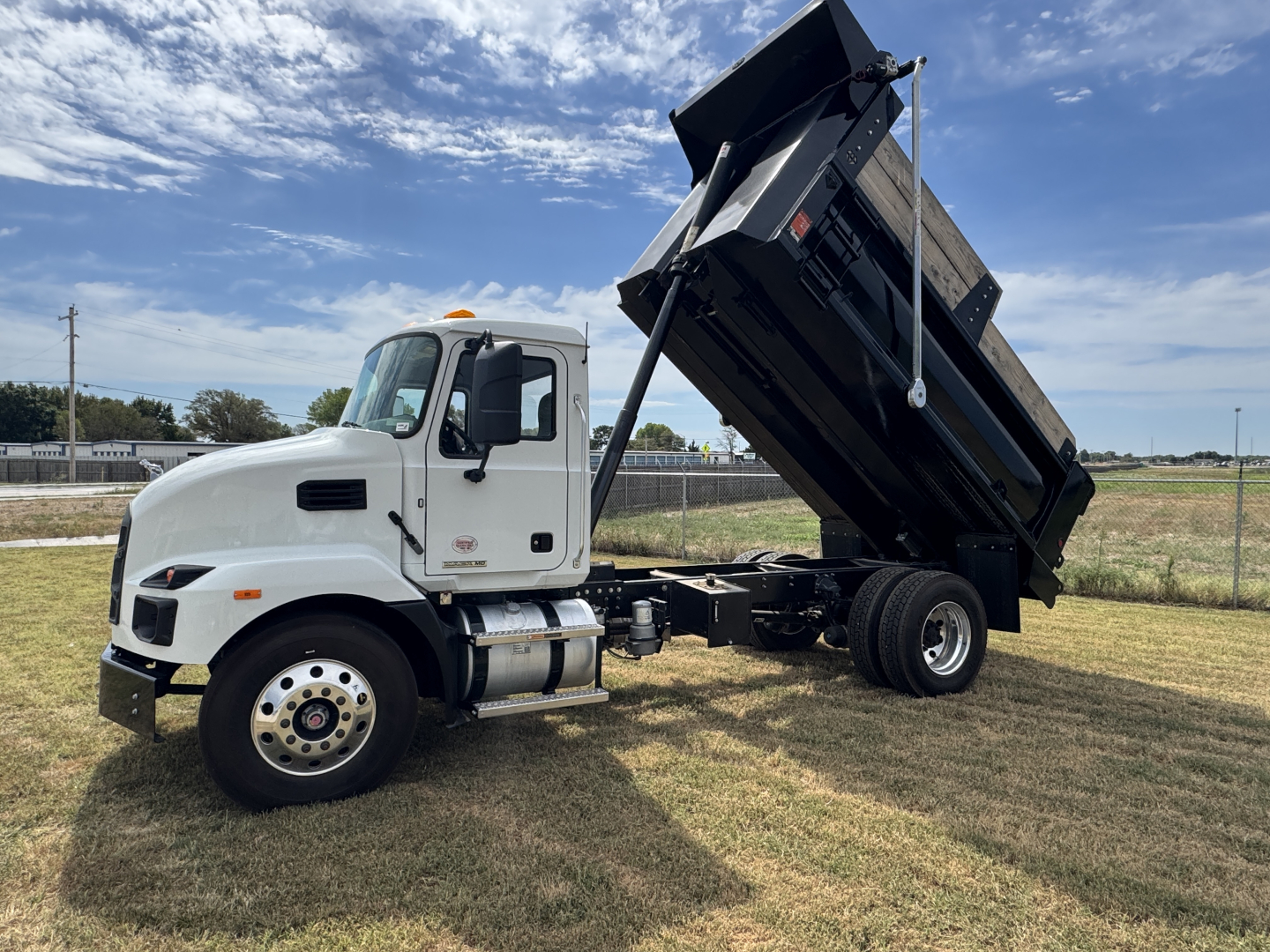 Dump truck cab and raised dump bed showing 2025 Mack MD7 chassis with white cab and black hydraulic bed in a field.
