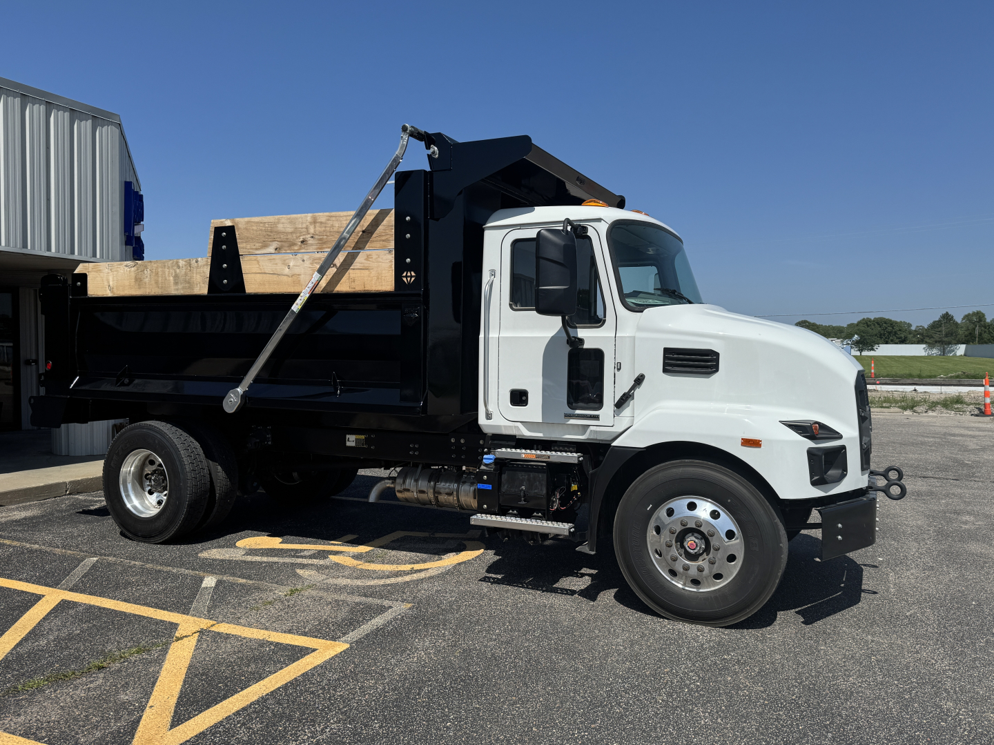 Dump truck side view showing white cab and black dump body with wooden bed and hydraulic lift.