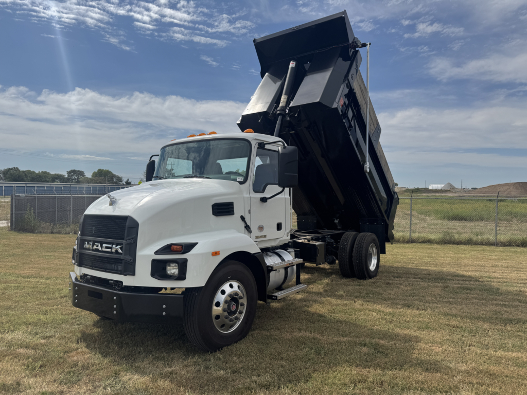 White Mack dump truck with raised dump body in a field, cab shows MACk logo on grille.