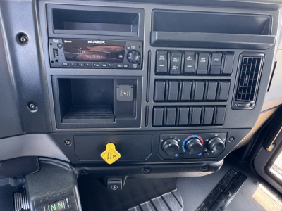 Mack MD7 dash and center console showing radio, numerous switch panels, climate controls, and a yellow hood release knob.