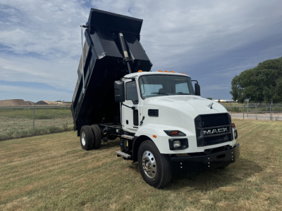 Mack MD7 dump truck with white cab and raised black dump bed, side view showing front grille and fog lights.
