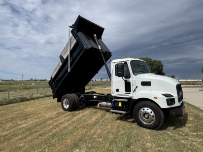 Dump truck (Mack MD7) with dumping bed raised, white cab, black dump body, side view showing hydraulic system and front wheels.