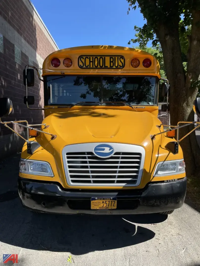 School bus front view showing bright yellow body, large grille, and windshield with 'SCHOOL BUS' sign; mirrors extended on both sides.