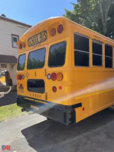 Yellow school bus rear view showing taillights, bumper, and windowed rear doors with 'SCHOOL BUS' sign above; vehicle identification numbers and reflective decals visible.