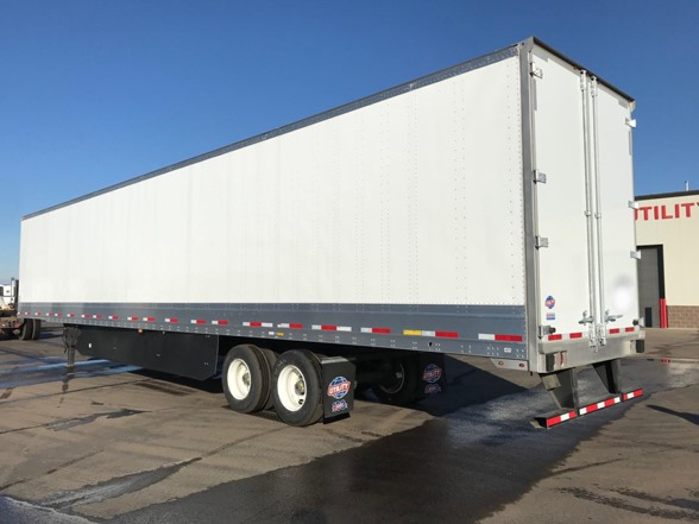 Utility 4000Dx trailer showing long rectangular dry van with tandem wheels and rear doors, white walls with reflective tape along lower edge.