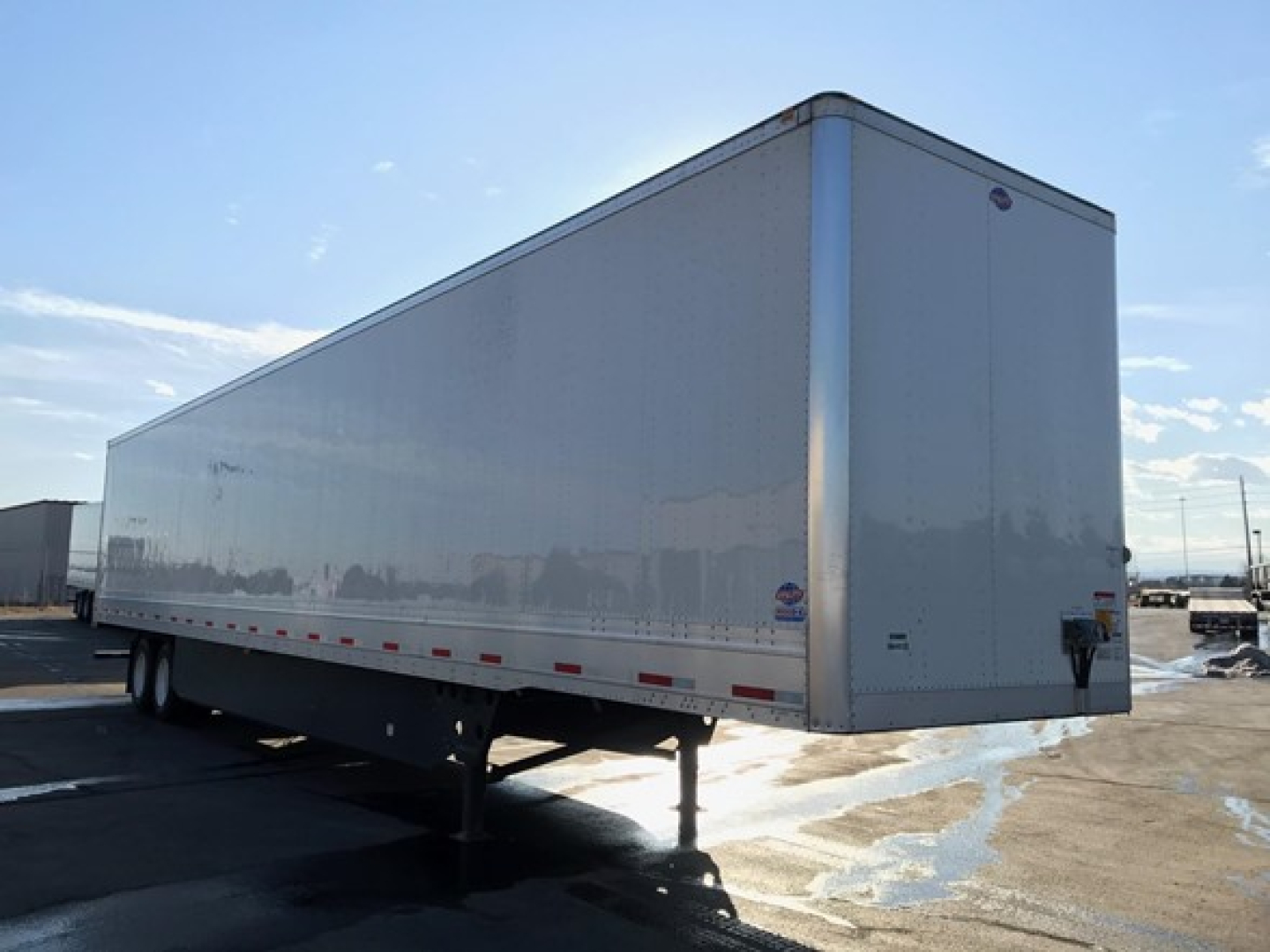 Long white Utility trailer in side view showing smooth exterior and dual rear wheels under a snow-dusted lot.