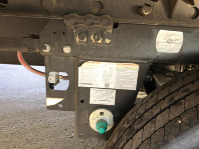 Trailer hitch area with label panel and a green circular cap, visible tire on the right. There are multiple warning stickers and a white label panel on the frame.