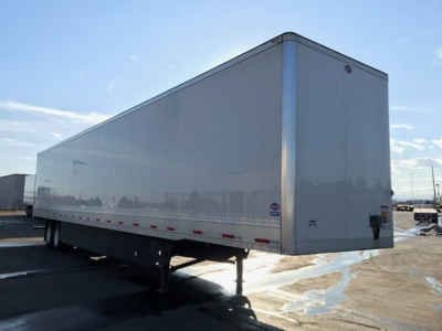 Trailer exterior showing a long, white utility box trailer with dual rear wheels and elevated landing gear, side panels clean with reflective striping.