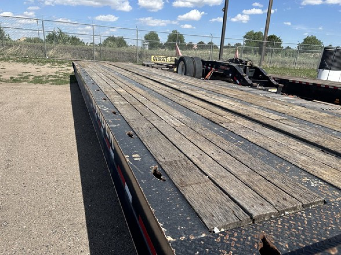 Flatbed trailer deck showing wooden planks and metal frame with wheel area in distance and open sky.