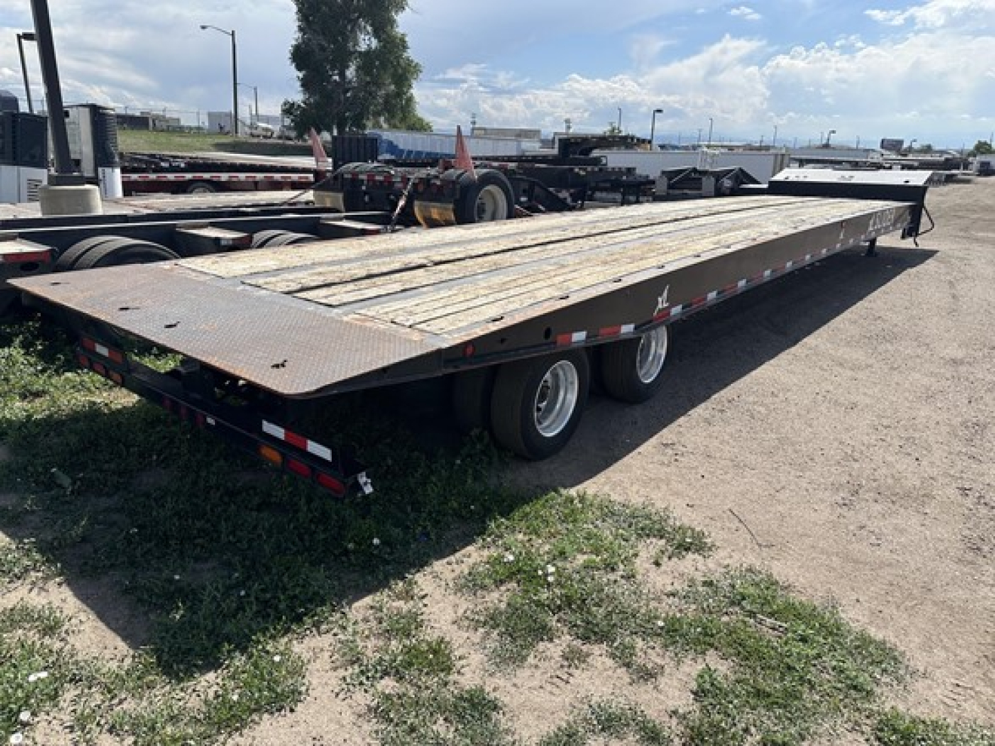 Flatbed trailer with dual rear axles, long rusty deck, and steel top; visible side rails and wheels under trailer; long recovery trailer for sliding axle use.