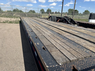 Flatbed trailer deck showing wooden planks and metal frame with wheel area in distance and open sky.