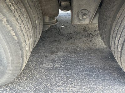 Trailer undercarriage showing dual rear axles with tires and a central wear plate; view between axles with ground surface visible.