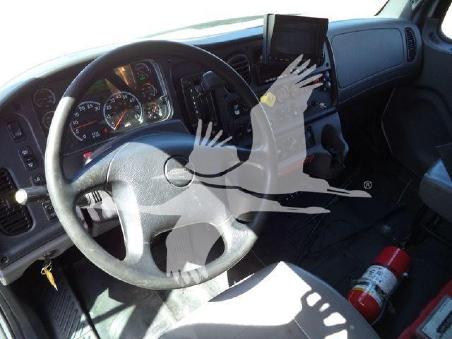 Cab interior of a Freightliner M2 106 truck showing steering wheel, dashboard, and a mounted tablet; a fire extinguisher lies on the floor.