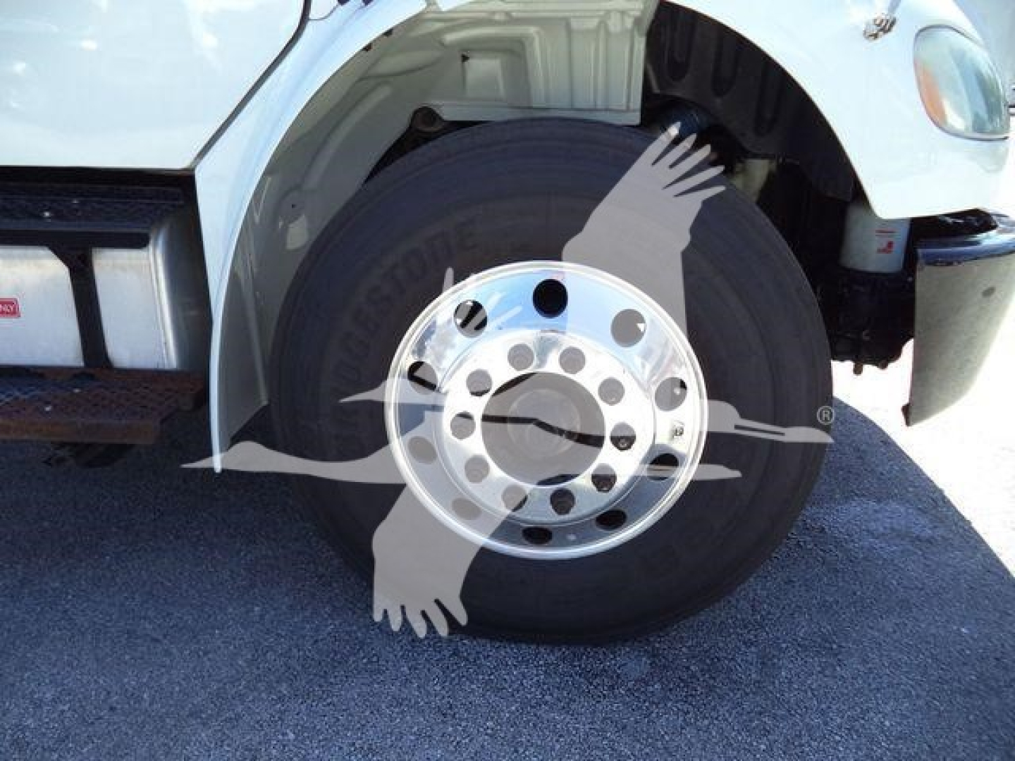 Wheel and front tire close-up on Freightliner M2 106 chassis showing steel wheel and tire with fender; partial cab and side panel visible