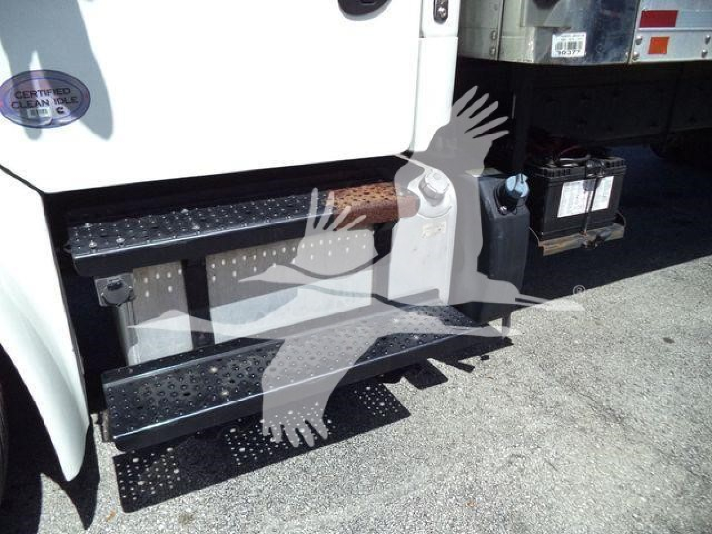 Step/footboard area of a 2019 Freightliner M2 106 truck showing rubberized steps and a side battery box with battery visible; partial front door with inspection badge.
