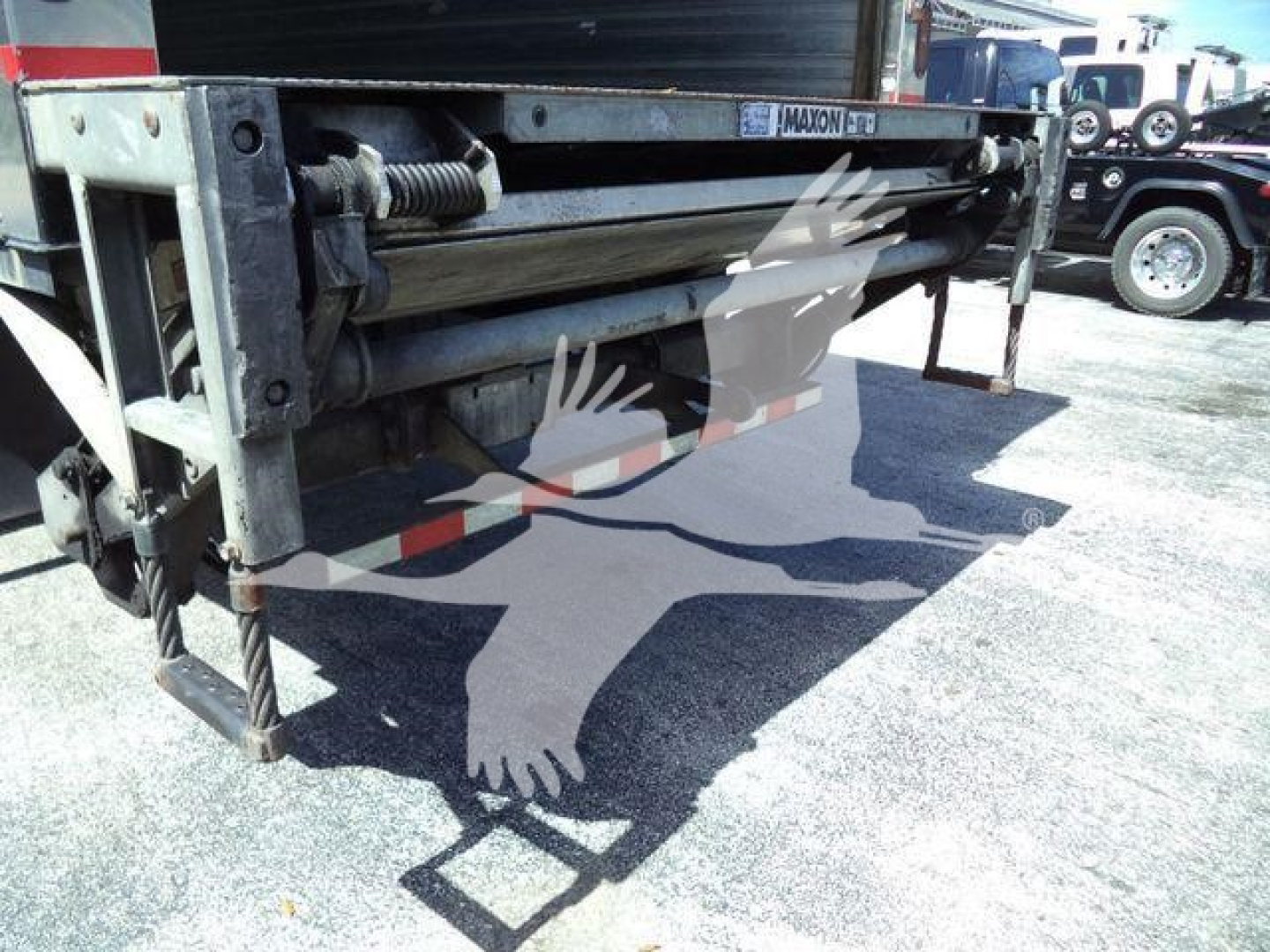 Freightliner M2 106 tailgate mechanism with guide rails and hydraulic components; visible metal frame and support hardware.