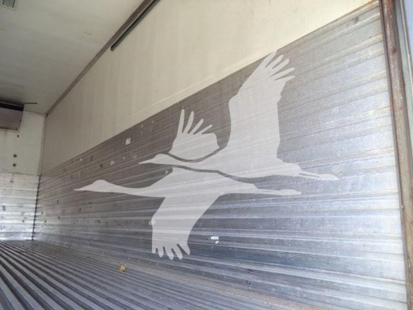Freightliner M2 106 trailer interior with silver ribbed wall and large white logo of two birds in flight on the side door.