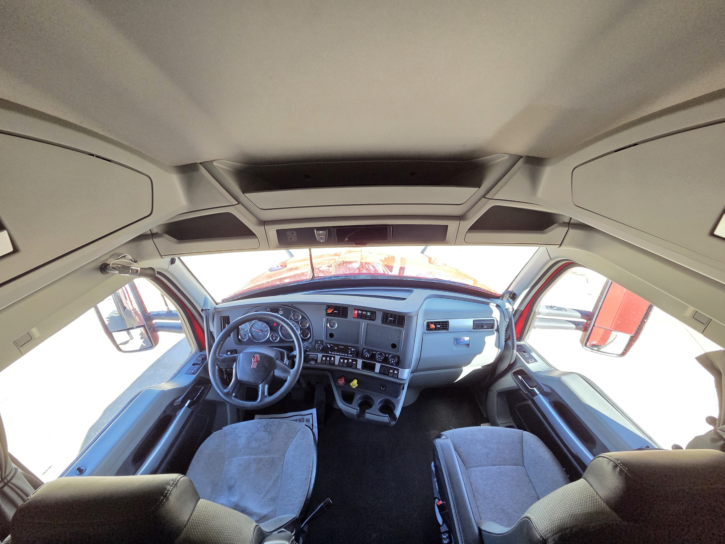 Kenworth T680 cab interior view from front windshield showing steering wheel, dashboard, and seats.