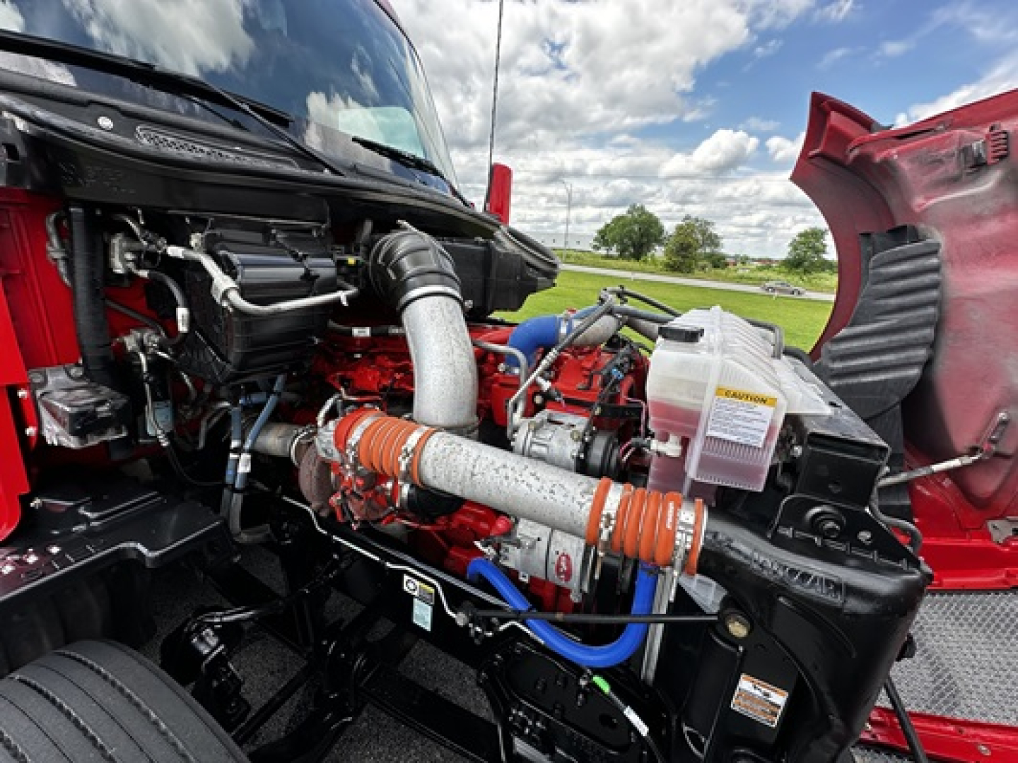 Kenworth T680 engine bay showing intake hose, coolant reservoir, and auxiliary components in a red truck with hood open.
