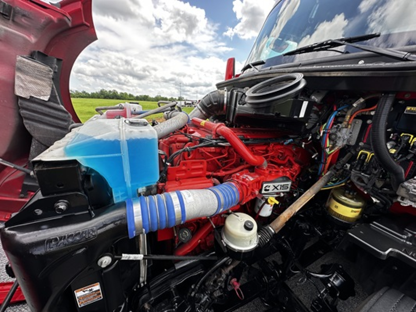 Kenworth T680 engine bay with red engine, blue coolant reservoir, blue hose, and various hoses and components visible