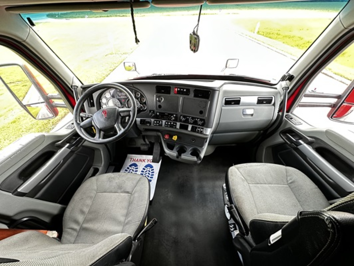 Kenworth T680 cab interior showing steering wheel, dashboard, and two front seats.