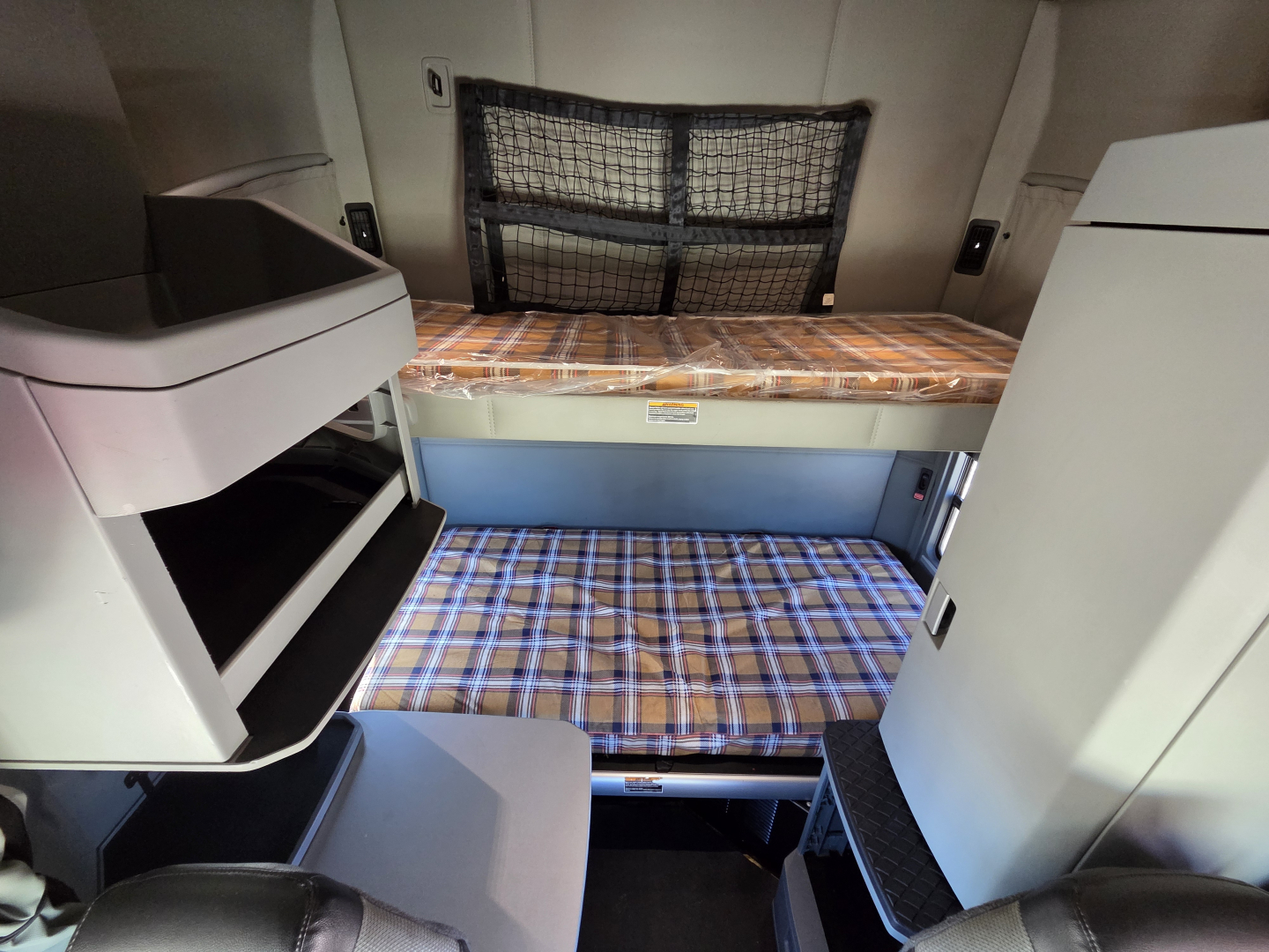 Interior sleeper cab of a 2022 Kenworth T680 showing bunk beds with plaid mattresses, cabinets, and storage net.
