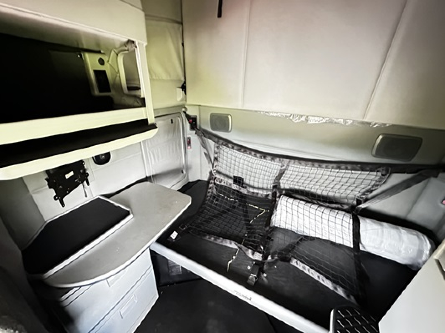 Kenworth T680 sleeper cab interior showing compact bunk area with netted storage and small desk area.